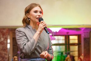 A woman speaks into a microphone, gives a lecture about business. Conference training seminar business presentation audience meeting.